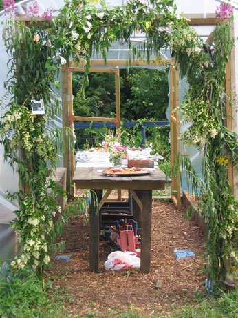  poly tunnel decorated with folliage, with wooden table and food in centre