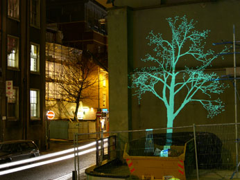 photograph of projected tree on outside of broadway building with street visible and skip infront