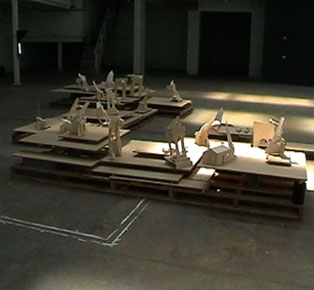 Photograph of Cristina Misuraca's installation of minature cardboard buildings upon stacked wood - with speaker underneath